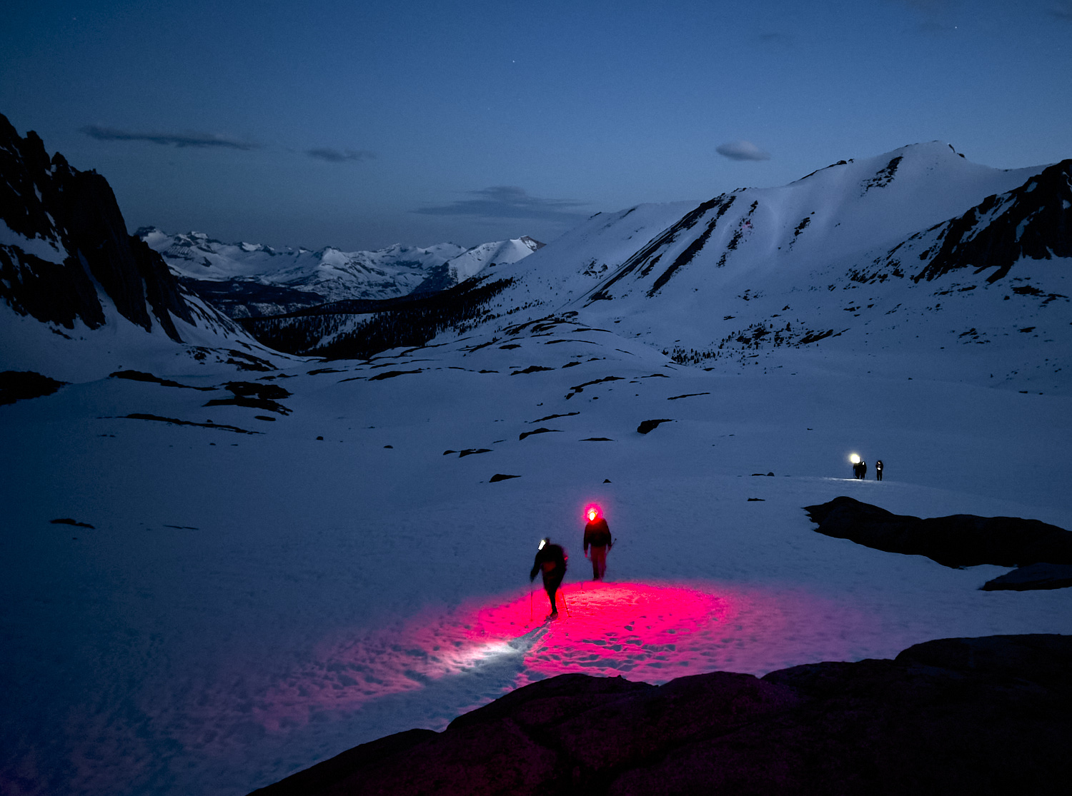 Hikers are ascending a slope at the base of Mount Whitney in the early morning before sunrise.