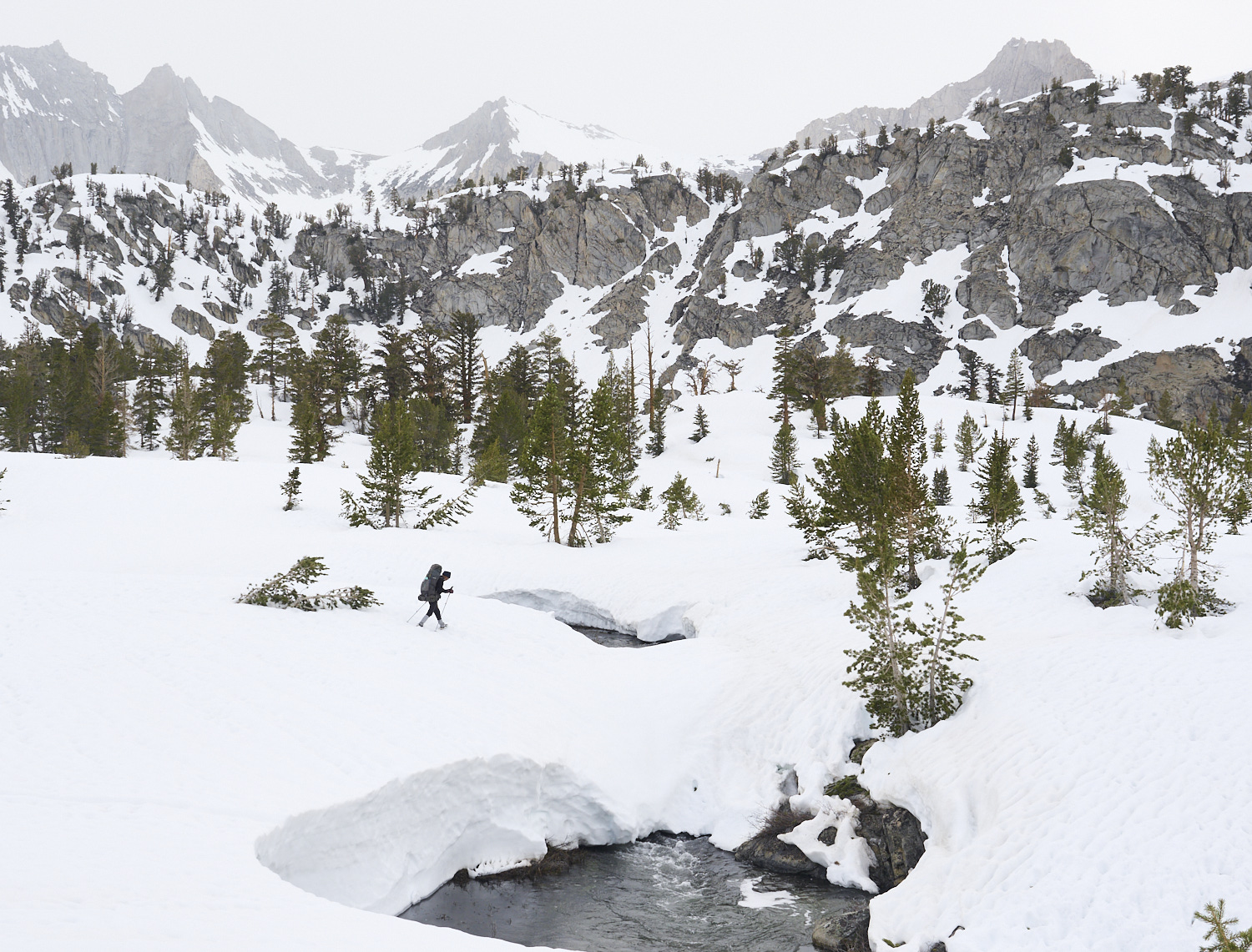 A hiker crosses a river on a snow bridge in Kings Canyon National Park.