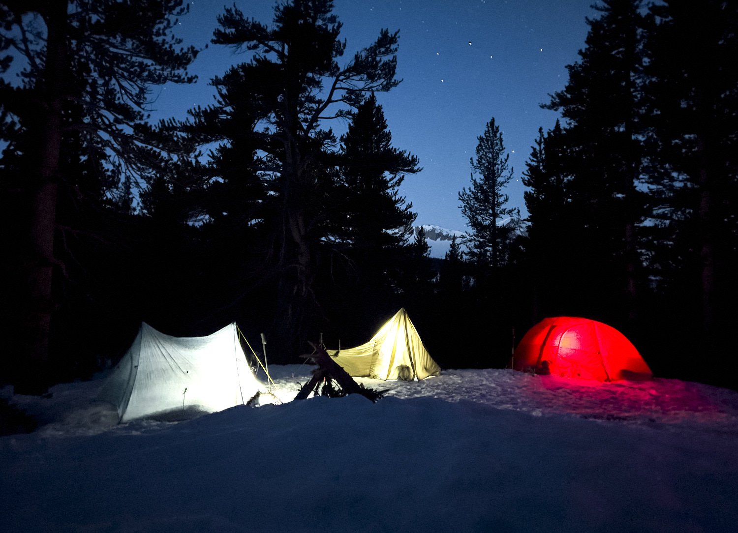 Illuminated tents in the early morning in a snow-covered forest in the Sierra Nevada.
