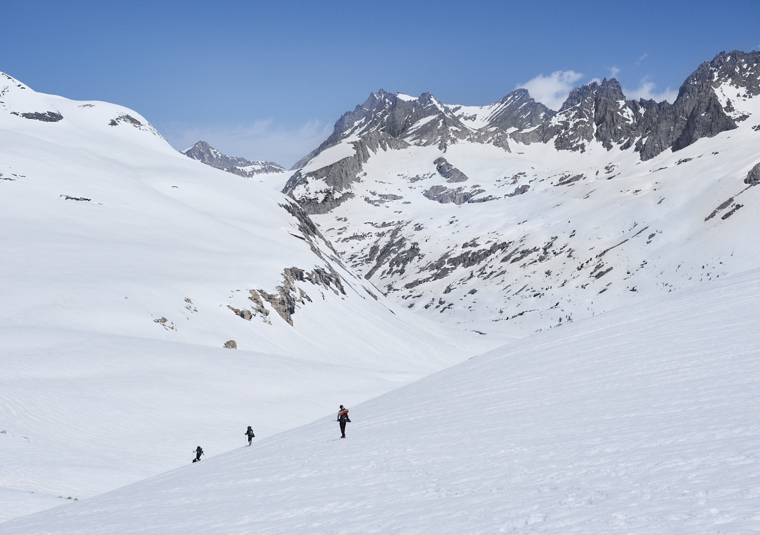 The snow covered Sierra Nevada from Mather Pass. Three hikers are descending from the pass into the valley.