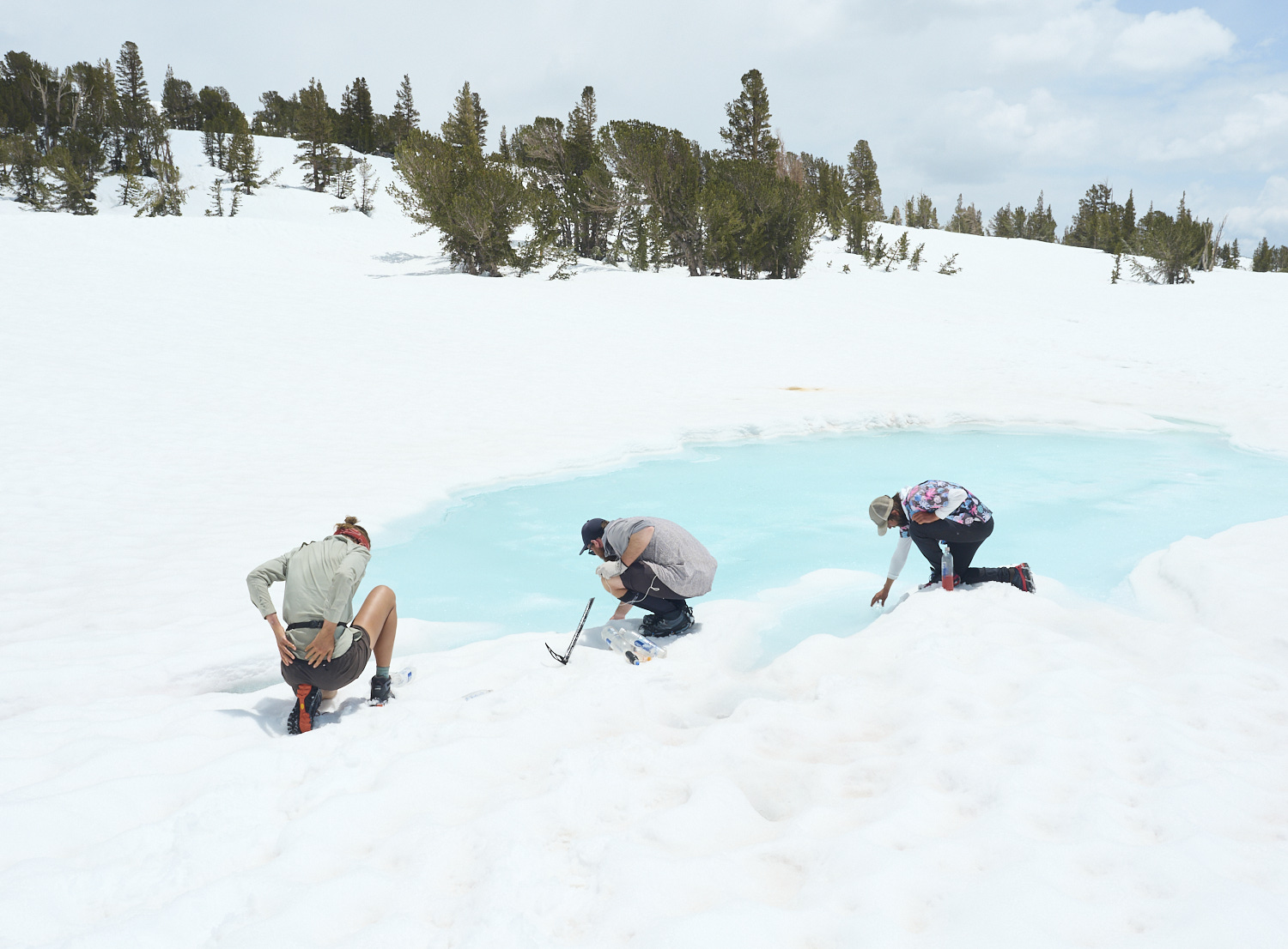 Hikers refill their bottles with water from a partially thawed lake.
