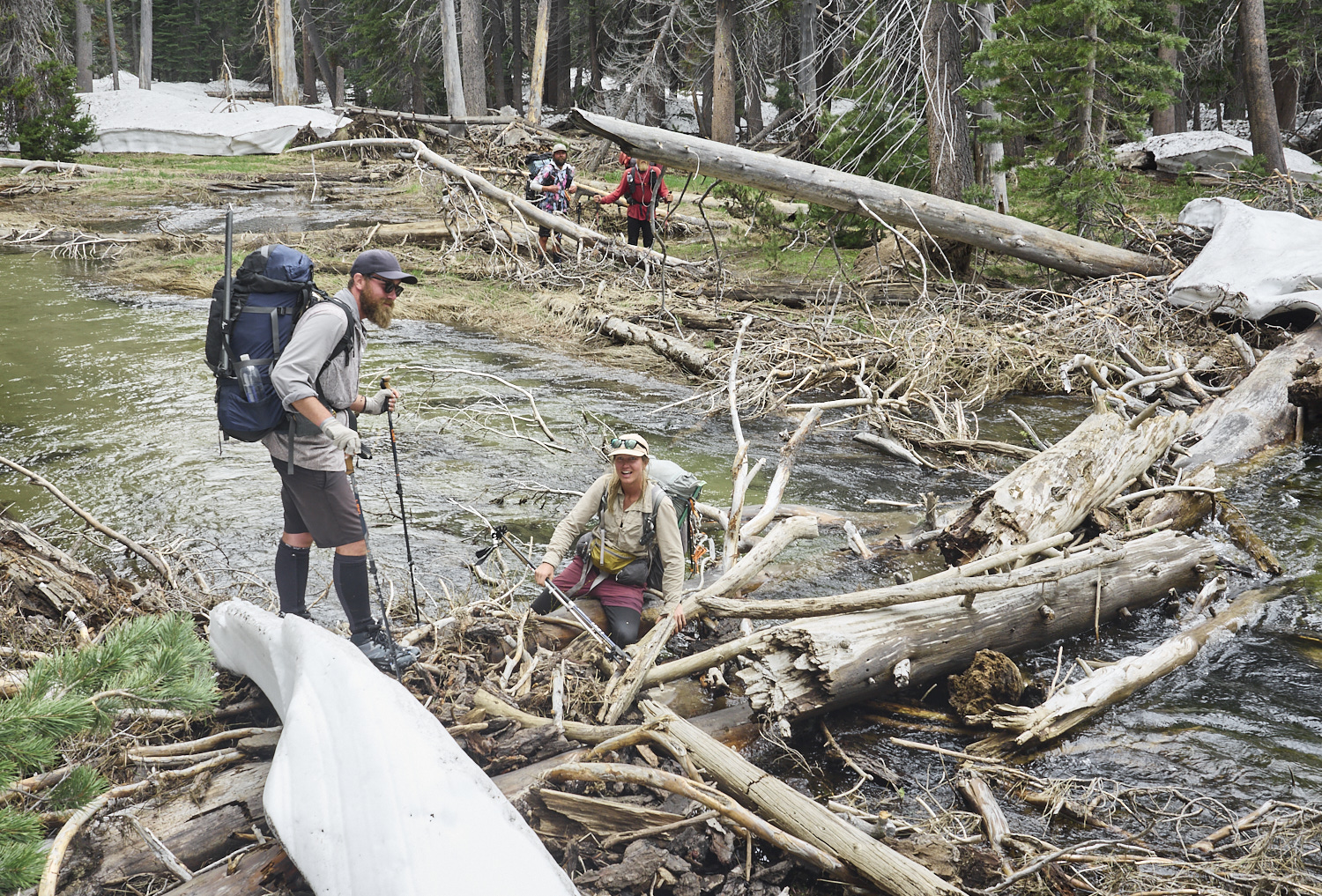 A hiker is sitting on a log in a river after she slipped on the wet log.