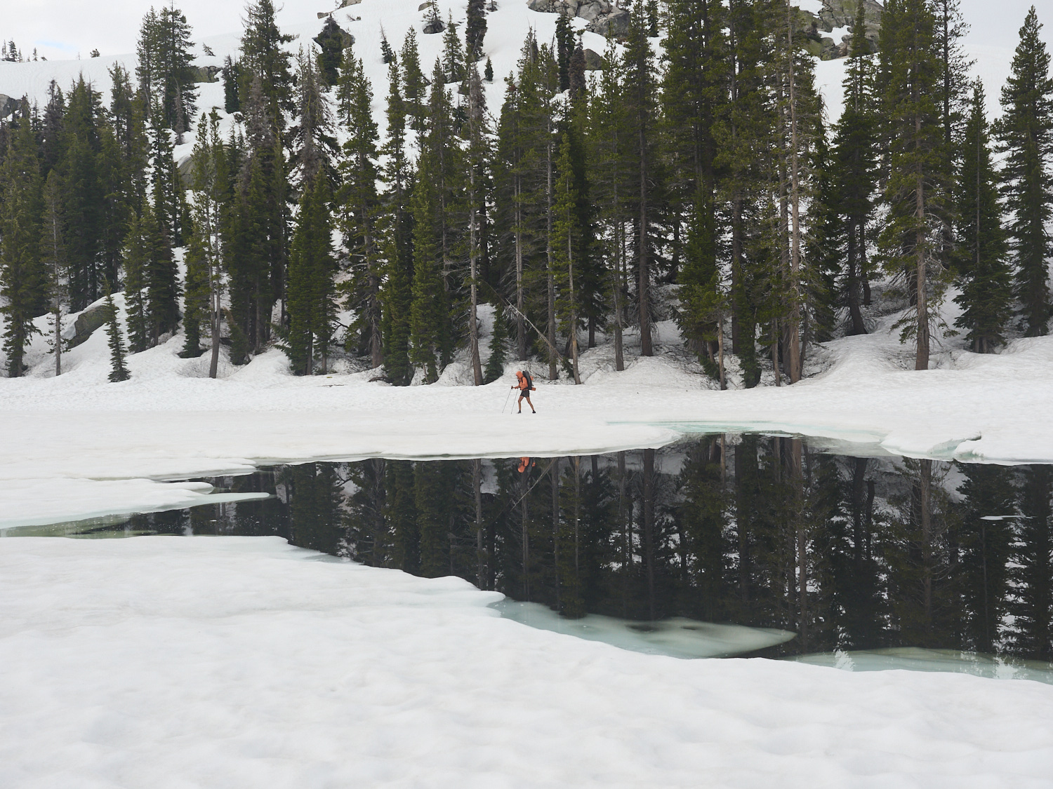 A hiker crosses the ice-covered surface of Wilma Lake in Yosemite National Park.