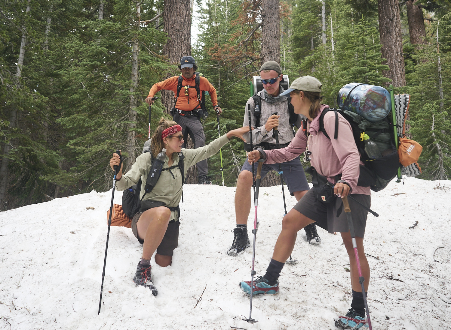 A hiker gets help from a companion to free her leg, which is almost completely stuck in a snow hole.