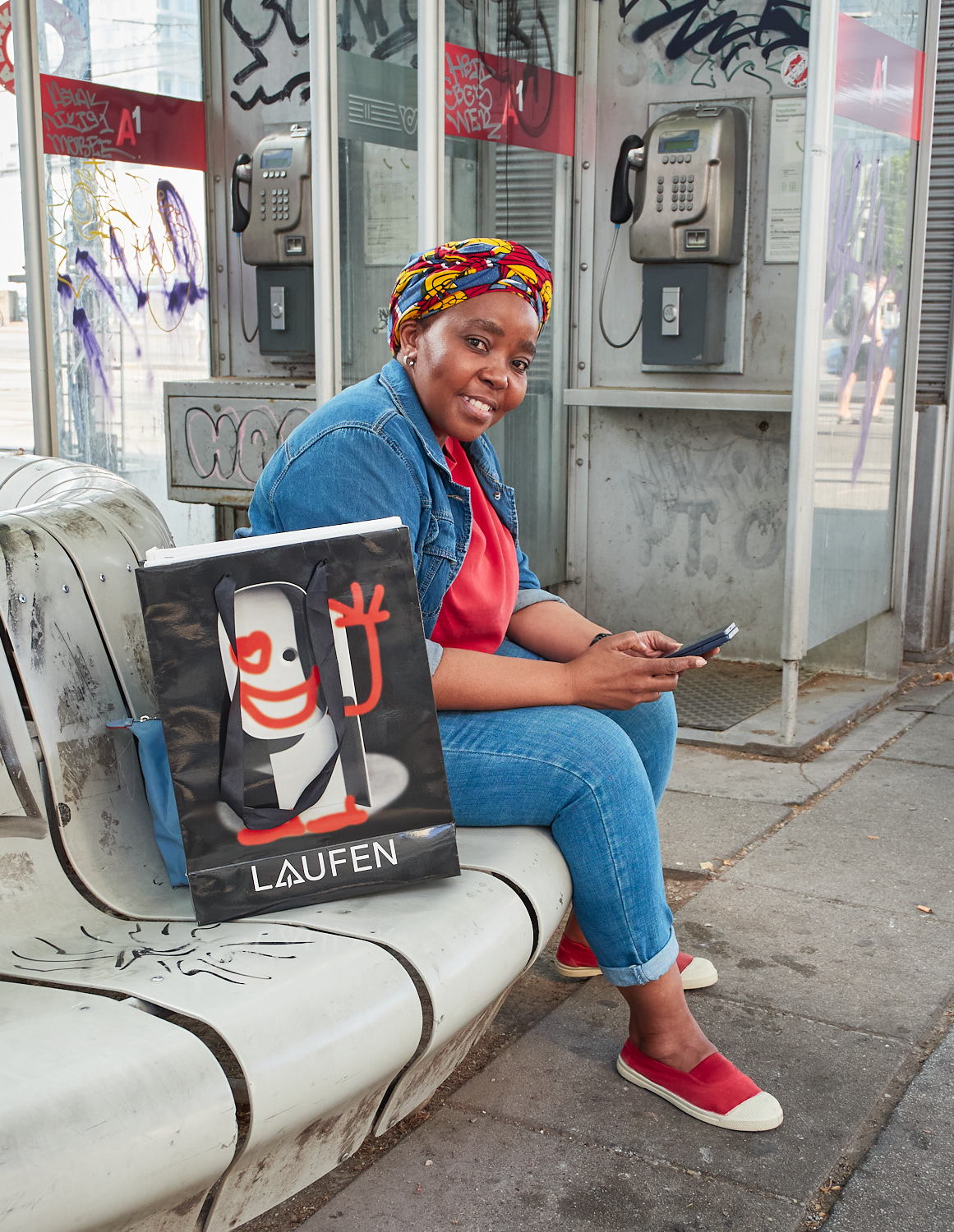 Eine Frau sitzt auf einer Bank vor einer Telefonzelle.