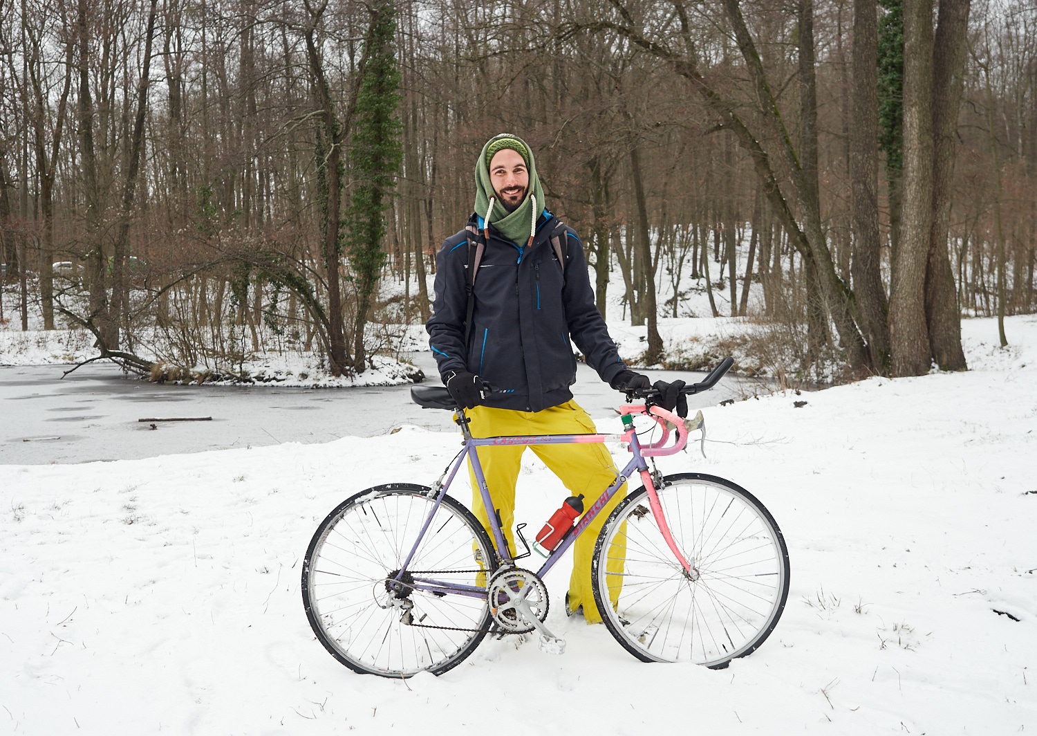 Ein junger Mann posiert mit seinem Fahrrad in einer winterlichen Waldlandschaft.